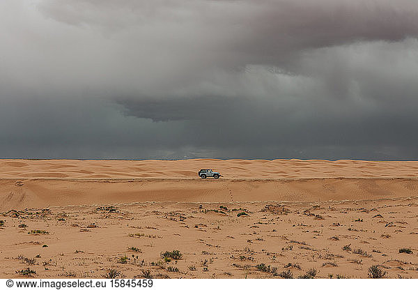 einsames Auto unter stürmischen Regenwolken bei einem Mikroausbruch in der Wüste