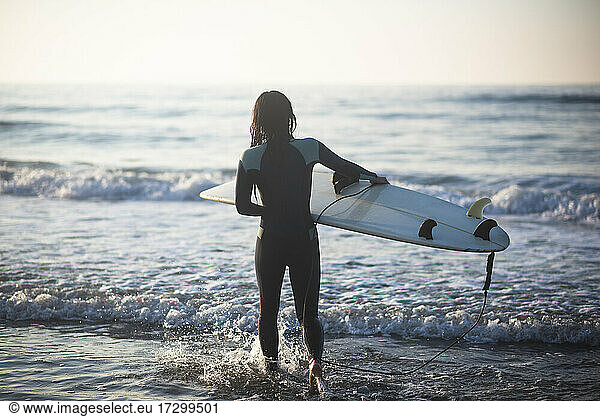 Einzelne asiatische Frau geht in der Morgendämmerung zum Surfen