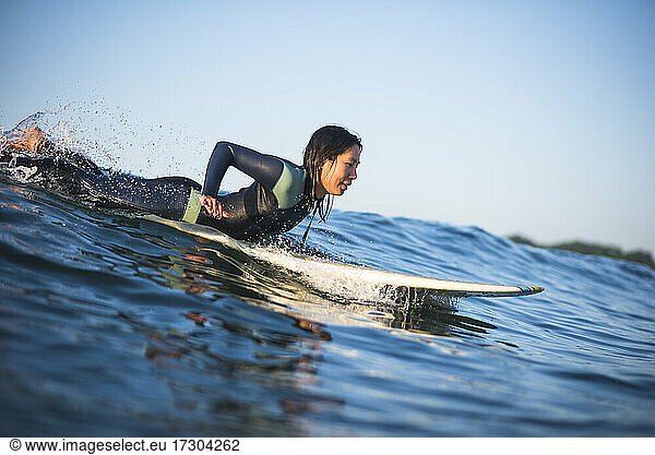 Einzelne asiatische Frau surft auf einer Welle an einem frühen Sommermorgen