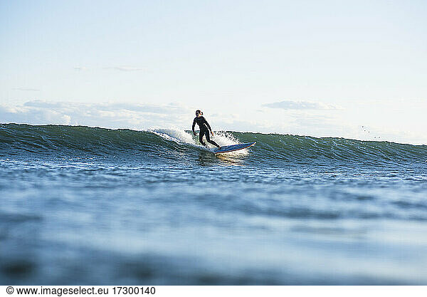 Einzelne Frau beim Surfen auf einer Welle im Sommer bei Sonnenuntergang