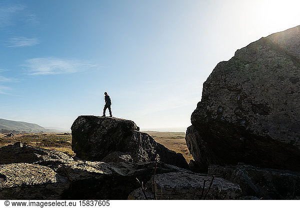 Einzelne Person  die sich vor blauem Himmel abhebt und auf einem großen Felsen steht