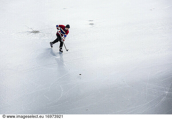 Eishockeyspieler beim Schlittschuhlaufen und Puckschießen auf dem Eis beim Teichhockey