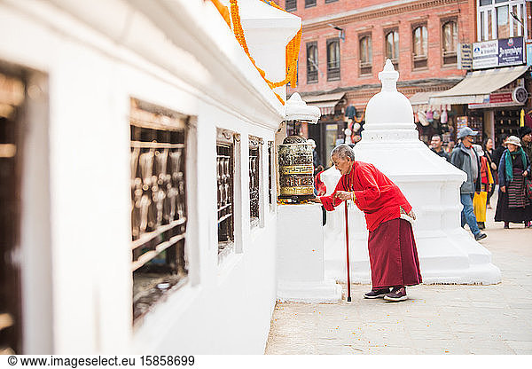 Elder Monk praying in front of prayer wheel