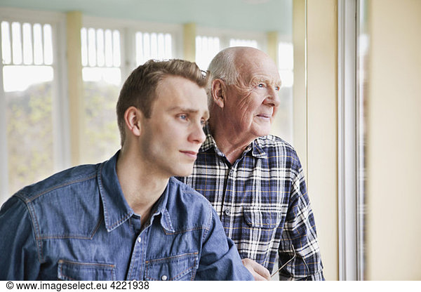 Elderly and younger man looking out through window
