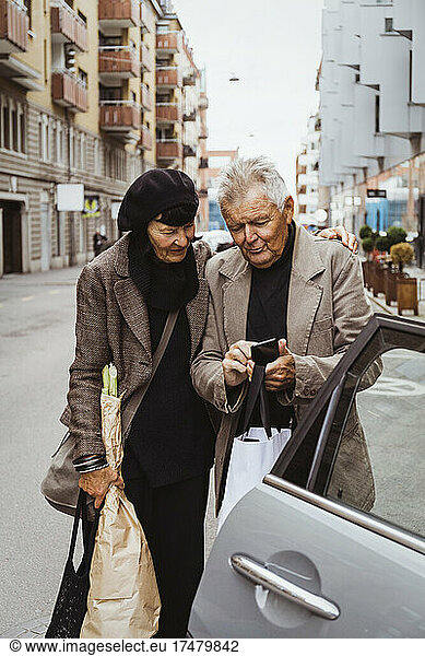 Elderly couple using smart phone by car on street in city