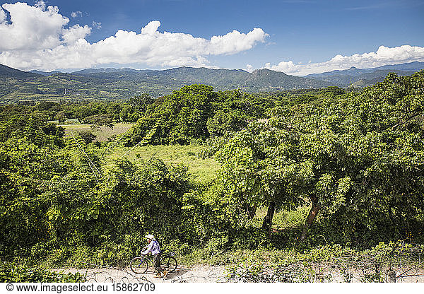 Elderly man pushing bike along dirt road  Guatemala.