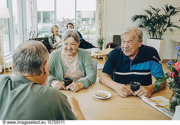 Elderly senior friends talking while sitting at dining table in nursing home