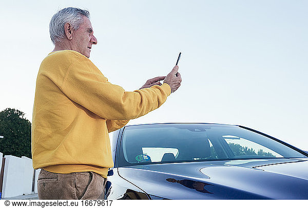 Elderly traveler using smartphone near car