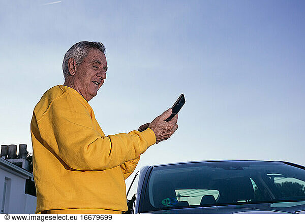 Elderly traveler using the GPS of his smartphone near the car
