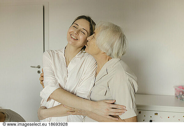 Elderly woman kissing granddaughter at home