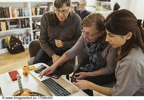 Elderly woman learning online shopping on laptop from female healthcare worker in nursing home