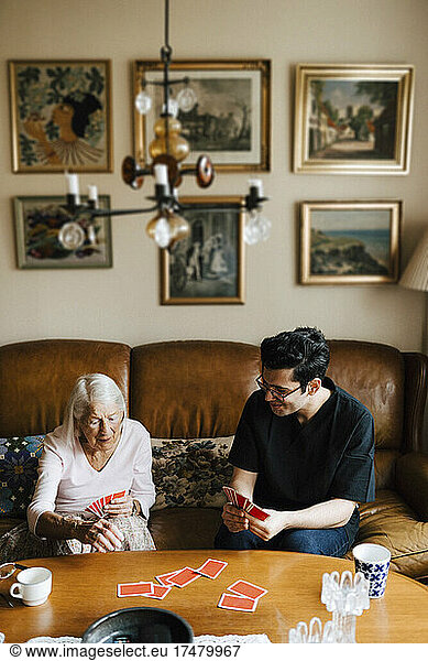 Elderly woman playing cards with male caregiver at table in living room