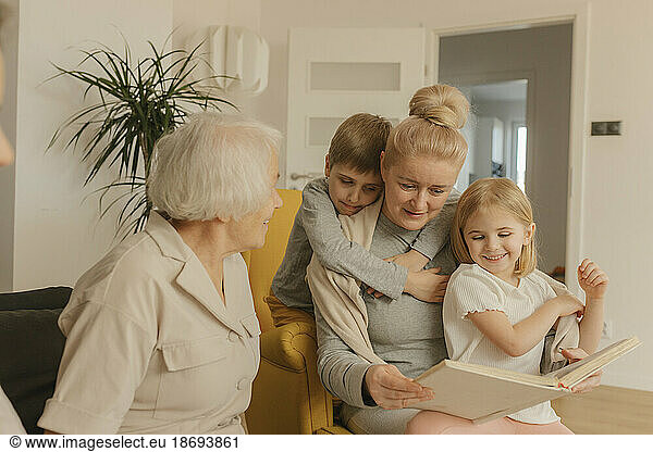 Elderly woman sitting with daughter and grandchildren watching photo album at home