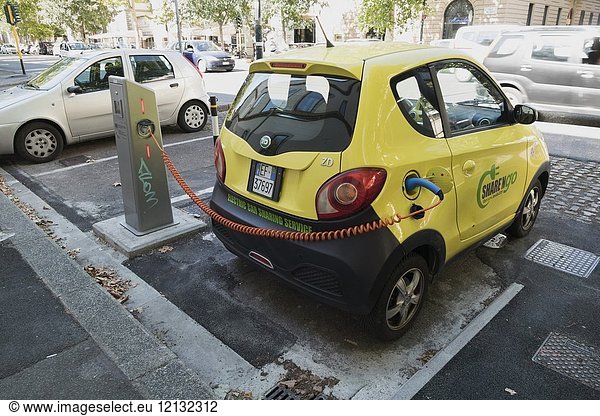 Electric yellow community share car recharging with orange spiral charging lead and parked in electric car sharing service bay in the business district of Florence Italy.