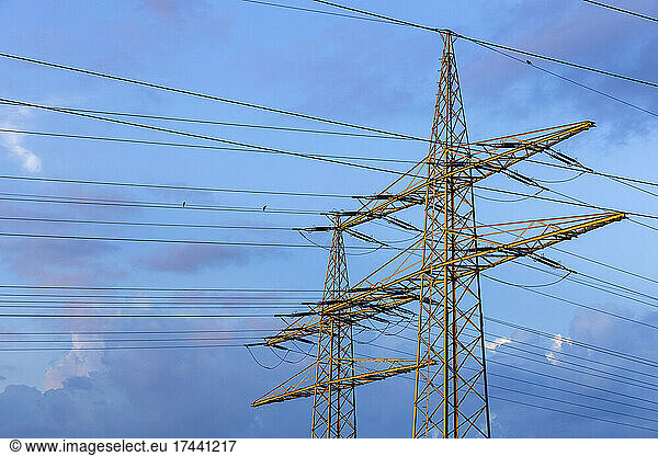 Electricity pylons standing against blue cloudy sky