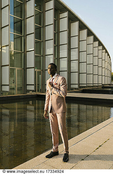 Elegant man wearing suit standing on footpath by pond