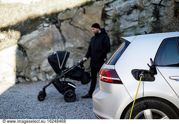 Elektroauto beim Aufladen  Mann mit Kinderwagen im Hintergrund