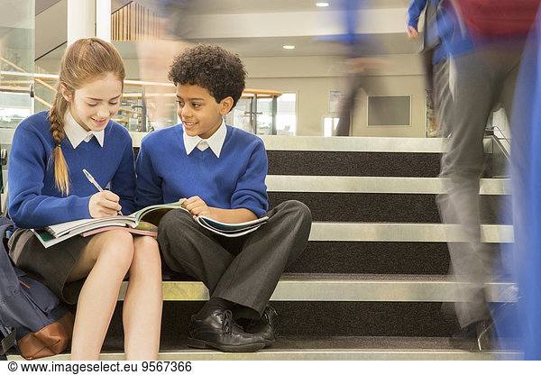 Elementary school children wearing school uniforms sitting on steps and writing in textbooks