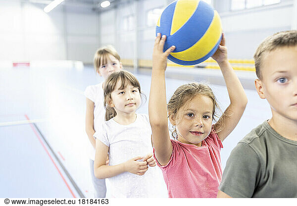 Elementary schoolgirl holding ball standing in line with friends at sports court