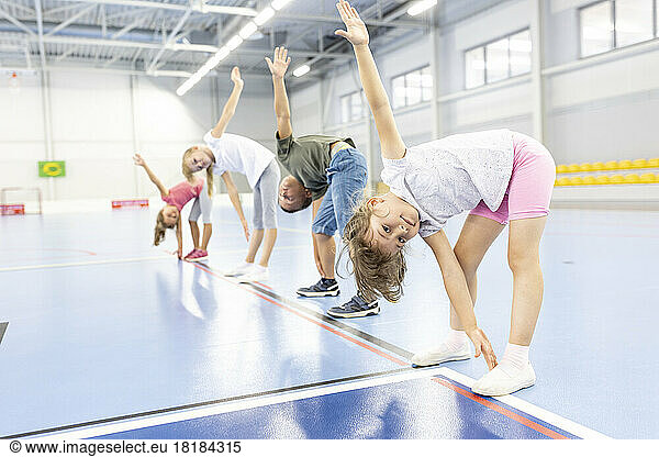 Elementary students doing stretching exercise with each other at school sports court