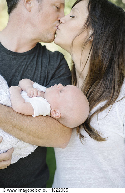 Eltern  die ein kleines Baby halten und sich küssen  ein Gruppenporträt.