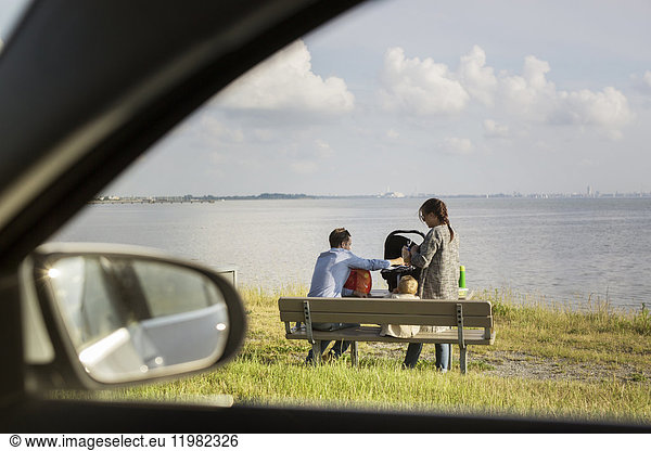 Eltern mit Sohn (18-23 Monate) auf einer Bank am Meer sitzend