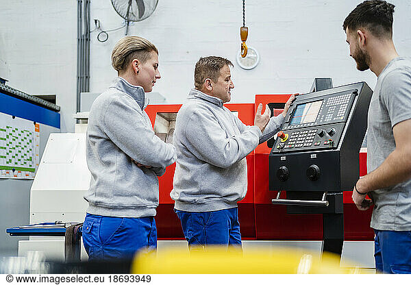 Employee explaining CNC machine to colleagues at factory