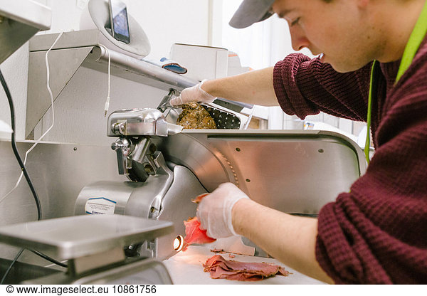 Employee in general store slicing meat in kitchen