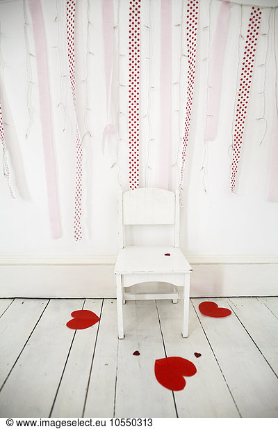 Empty chair in a photographers studio  fairy lights and red streamers on the wall  heart-shaped paper cut-outs on the white wooden floor.