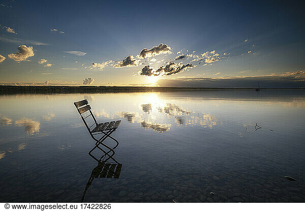 Empty chair standing in water at atmospheric sunset