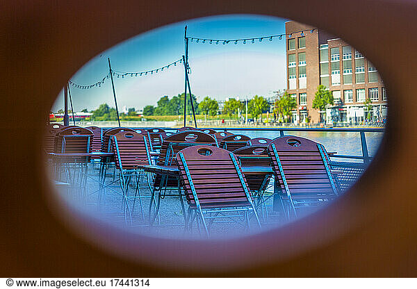 Empty chairs and tables on restaurant terrace seen through oval hole