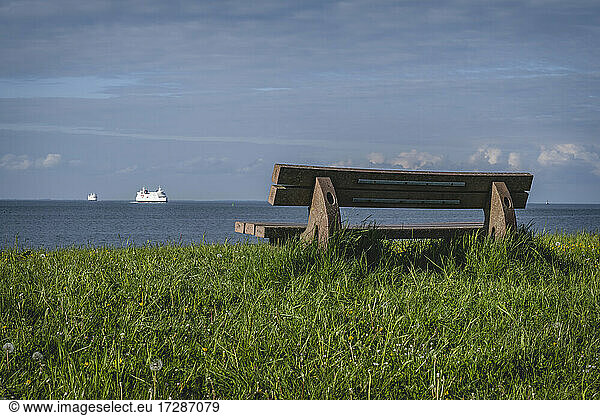 Empty coastal bench with ferries sailing in distant background