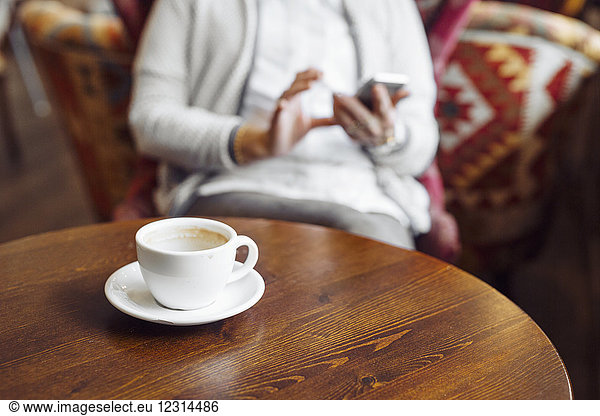 Empty coffee cup and woman using mobile phone in background