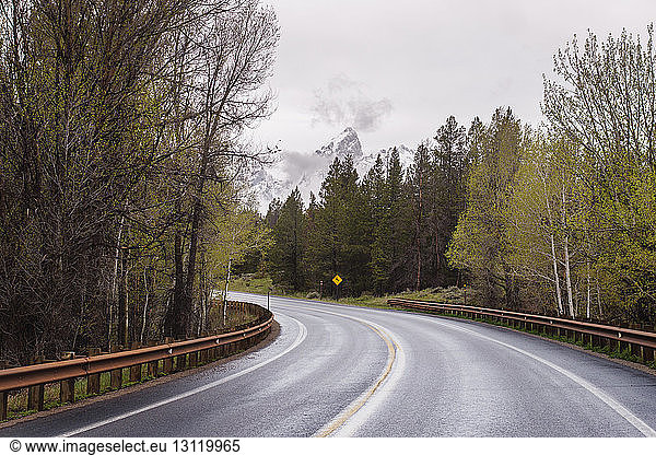 Empty country road amidst trees against sky at Grand Teton National Park