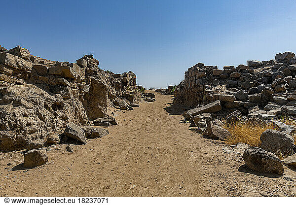 Empty dirt road amidst rocks under blue sky at Al-Ukhdud Archaeological Site in Najran  Saudi Arabia