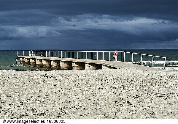 Empty jetty at beach against cloudy sky