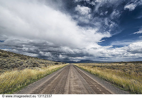 Empty road amidst field against cloudy sky