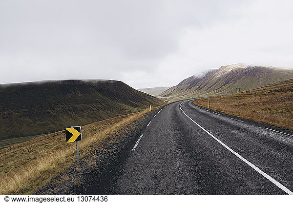 Empty road amidst mountains against cloudy sky