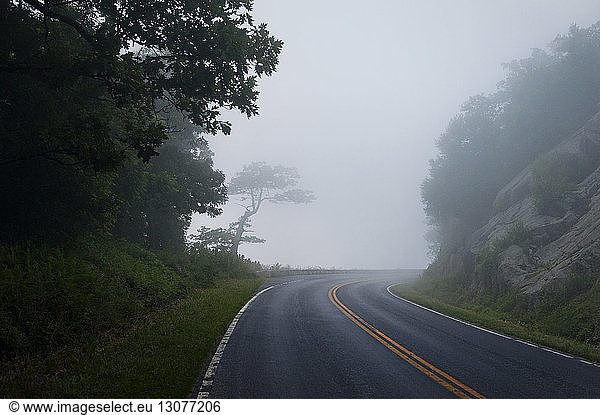 Empty road amidst mountains against sky during foggy weather