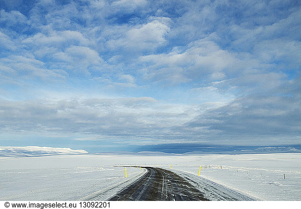 Empty road amidst snowy field against sky