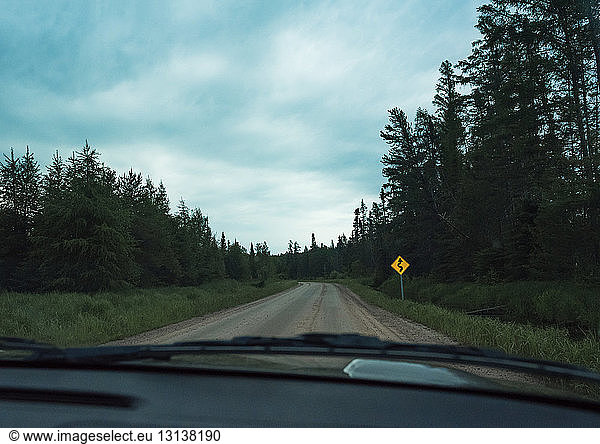 Empty road amidst trees against cloudy sky seen through windshield
