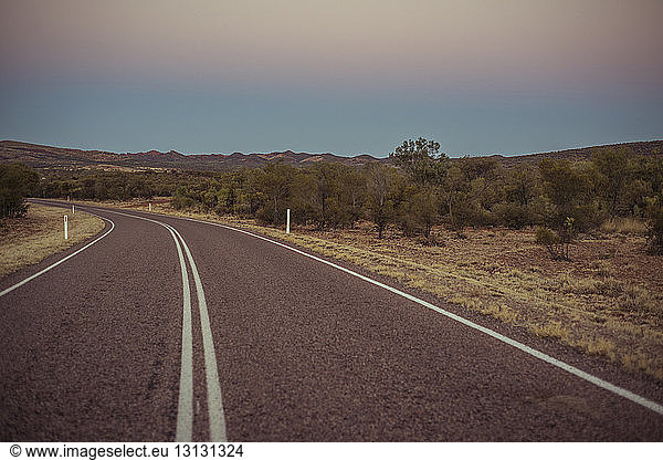 Empty road at desert against clear sky during sunset