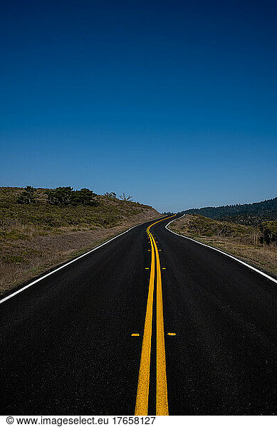 Empty road leading out to clear blue sky on California coast
