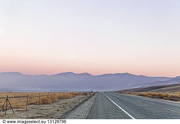 Empty road leading towards mountains against clear sky