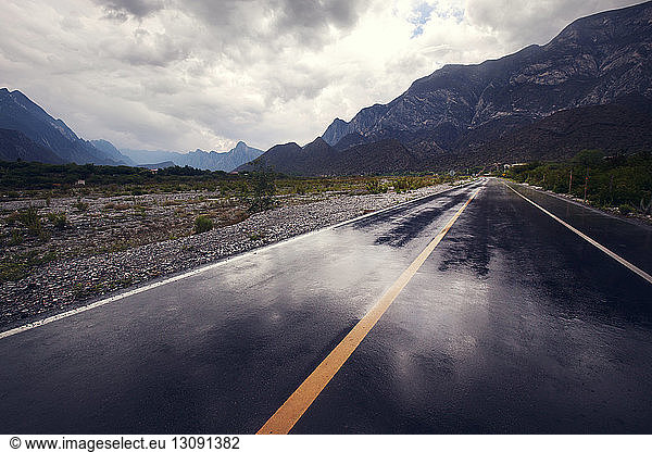 Empty road leading towards mountains against cloudy sky