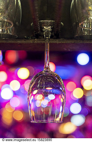 Empty wineglass hanging over counter with bokeh lights in background