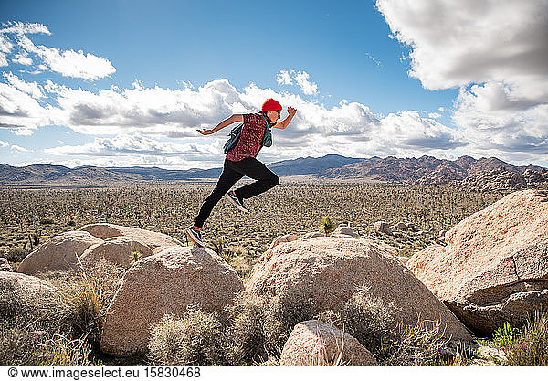 Energetic teen jumping across rock in Joshua tree national park