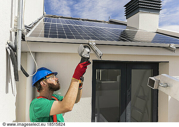 Engineer cutting metal under solar panels with hand saw on roof