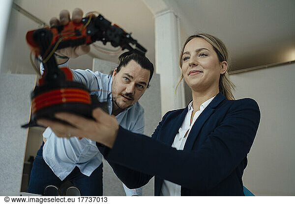 Engineer discussing with colleague over robotic arm model in office