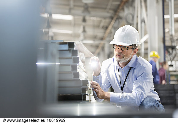 Engineer examining steel parts with flashlight in factory